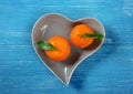 Two tangerines in a heart shaped plate on blue wooden table background Royalty Free Stock Photo