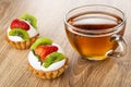 Two tartlets with cream, strawberry and kiwi, cup with tea on wooden table