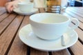 Two teacups and French press on the table, blurred woman behind.