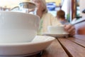 Two teacups and French press on the table, blurred woman behind.