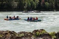 Two teams of people rafting in equipment, lifejackets and yellow helmets on blue inflatable boats on a mountain river with rapids