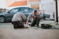 Two technicians kneel and repair a car panel in a driveway using hand tools Royalty Free Stock Photo