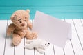 Two teddy bear sitting on white wooden floor in blue-green background with blank note Royalty Free Stock Photo