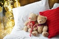 Two teddy bears siting on the bed with red candys near christmas tree.