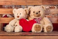 A couple of teddy bears are sitting on a bench next to a heart made of soft toys