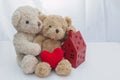 Two teddy bears sitting with red heart yarn and red house on white fabric.