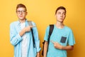 Two teen guys point at each other with their thumbs, blame and do not want to admit their guilt, isolated on a yellow background Royalty Free Stock Photo