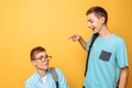 Two teenage friends, one guy humiliates the other, popular humiliates the unpopular, on a yellow background Royalty Free Stock Photo