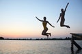 Two teenage girls jump in the evening from the pier into the water