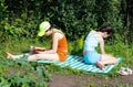 Two teenage girls sit on a summer sunbed in the garden. One is playing and the other is reading a book Royalty Free Stock Photo