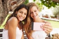 Two Teenage Girls Sitting On Bench Taking Selfie In Park Royalty Free Stock Photo