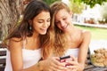 Two Teenage Girls Using Mobile Phone Sitting On Park Bench Royalty Free Stock Photo