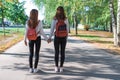 Two teenage girls walk in summer in park, walk after school and college, hold hands, best friends return home after