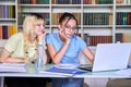 Two teenage schoolgirls students sitting with a laptop in the library Royalty Free Stock Photo