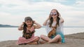 Two teenage are sitting on a sandy beach near the sea. They have two dogs.