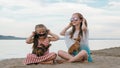 Two teenage are sitting on a sandy beach near the sea. They have two dogs.