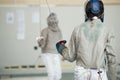 Two teenager fencers in white protective clothes fighting on the fencing tournament