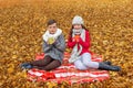 two teenagers drinking tea sitting on a plaid in an autumn forest field