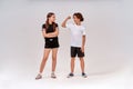 Two teenagers exercising together. Boy showing his biceps to a cute girl, they standing isolated over grey background in