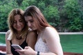 Two teenagers watching a video in a cell phone, and laughing, sitting in a boat. Caucasian Girls friends addicted to the Royalty Free Stock Photo