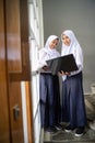 two teenagers wearing headscarves in school uniforms carrying a laptop