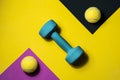 Two tennis balls and a blue dumbbell on a lilac, black and yellow background. Sport, activity, fitness Royalty Free Stock Photo