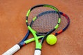 Two tennis rackets and yellow tennis ball lie on the clay court