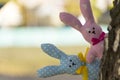 Two textile toys hare peeking from behind a birch tree trunk. Close-up. Blurred background