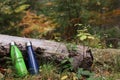 Two thermo bottles near log in autumn forest