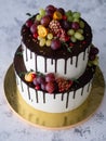 Two-tiered white cake with fresh fruits - pomegranate, green and red grapes, kumquat, cranberries, thyme sprigs - and chocolate Royalty Free Stock Photo