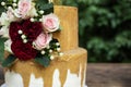 Two tiered white and gold wedding cake with red and pink roses and ruscus leaves Royalty Free Stock Photo