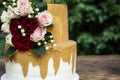 Two tiered white and gold wedding cake with red and pink roses and ruscus leaves Royalty Free Stock Photo