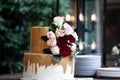 Two tiered white and gold wedding cake with red and pink roses and ruscus leaves on a wooden vintage cart Royalty Free Stock Photo