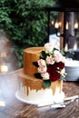 Two tiered white and gold wedding cake with red and pink roses and ruscus leaves on a wooden vintage cart Royalty Free Stock Photo