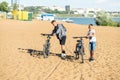 Two tired boys dragging bicycles on sandy city pond beach at evening Royalty Free Stock Photo