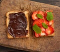 Two toasts with chocolate paste and fresh ripe red strawberries on a brown wooden board Royalty Free Stock Photo