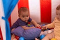 Two toddlers playing with balls sitting inside circus tent at home