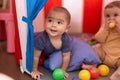 Two toddlers playing with balls sitting inside circus tent at home