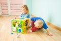 Two toddlers sitting on a floor near large toy