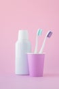 Two toothbrushes in a pink cup and mouthwash in a bottle on pink background, oral hygiene concept