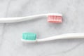 Two toothbrushes with pink and turquoise blue bristle on marble background.
