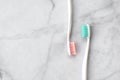 Two toothbrushes with pink and turquoise blue bristle on marble background.