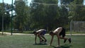 Two topless athletes doing burpees in unison on the grass.