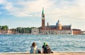 Two tourist girls sitting on the waters edge and enjoying the idyllic scene on Grand Canal in Venice