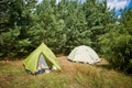 Two tourist tents in the forest. Green and white cover. Active rest in the summer on the nature.