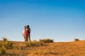 Two tourists with backpacks are standing on a hilltop against a blue sky. Summer evening, sunset Royalty Free Stock Photo