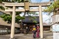 Two tourists dressed in geisha colorful kimono standing under stone Torii Gate in Higashi Chaya Geisha district.