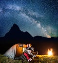 Two tourists looking to the shines starry sky and Milky way near shining tent in the camping at night near campfire