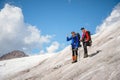 Two tourists, a man and a woman with backpacks and cats on their feet, stand on the ice against the background of the Royalty Free Stock Photo