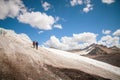 Two tourists, a man and a woman with backpacks and cats on their feet, stand on the ice in the background of the Royalty Free Stock Photo